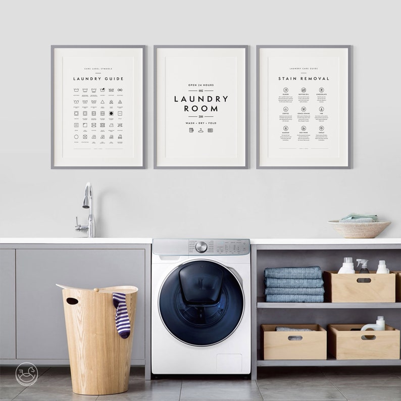 May include: A laundry room scene featuring a washing machine, wooden hamper, and three framed prints. The prints display laundry symbols, "Laundry Room" text, and stain removal instructions. The room has a modern, minimalist design.