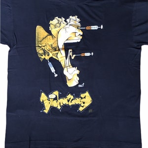 May include: Dark navy blue t-shirt featuring a surreal graphic design. The design includes a stylized face with syringes labeled "Ignorance" and "Racism." Below, the word "Dichotomy" is written in a graffiti-style font. The shirt is a vintage item.