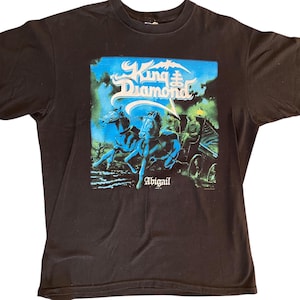 May include: Black t-shirt featuring a graphic design with the text "King Diamond" in a stylized font. The design includes a carriage pulled by two blue horses, with the name "Abigail" below.