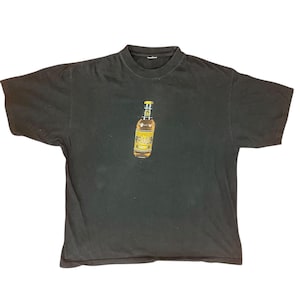 May include: Black t-shirt featuring a graphic of a beer bottle with the word "PRIMUS" in yellow. The bottle has a yellow and gold label. The t-shirt is a crew neck style.