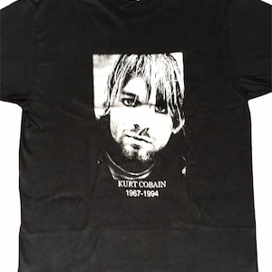 May include: Black t-shirt featuring a white image of Kurt Cobain and the text "Kurt Cobain 1967-1994".