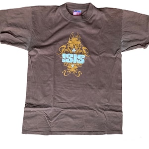 May include: A brown t-shirt with a gold and blue graphic design featuring the word "ISIS" in a stylized font.