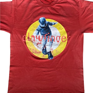 May include: Red t-shirt with a yellow circle graphic featuring a person in a blue sweater and black shoes. The text "Clawfinger" is printed in red letters inside the circle.