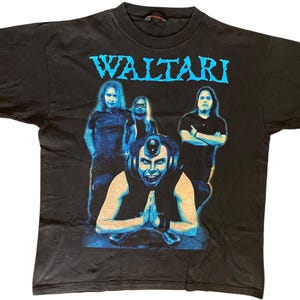 May include: Black t-shirt with the band name "WALTARI" in blue lettering. The graphic depicts four band members in blue and black. One figure in the foreground wears headphones and clasps their hands together.