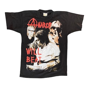 Könnte beinhalten: Schwarzes T-Shirt mit einer Grafik von drei Musikern und dem Wort "ANARCHY" in Rot darüber. Die Worte "WILL BEAT" sind darunter in Rot gedruckt. Das T-Shirt hat einen Vintage-Look.