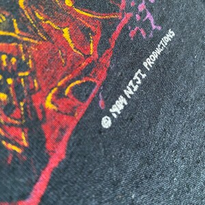 May include: Close-up of a black t-shirt with a red, yellow and purple graphic design. The text "1994 NIGHT PRODUCTIONS" is printed in white on the bottom right corner of the shirt.
