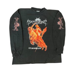 Könnte beinhalten: Schwarzes Langarmshirt mit einer Grafik einer Figur, die ein feuriges Tier reitet, mit dem Wort "Stormblade" darunter. Die Ärmel haben ein rot-weißes Design. Das Shirt hat das Wort "Demivix" in Weiß über der Grafik.