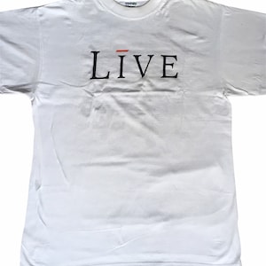 Może przedstawiać: Biała koszulka z nadrukiem słowa "LIVE" czarnymi literami z czerwoną linią nad "I".