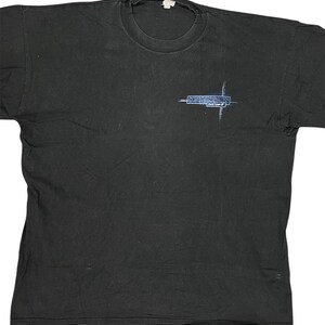 Könnte beinhalten: Ein schwarzes kurzärmeliges T-Shirt mit Rundhalsausschnitt. Auf der linken Brust befindet sich eine kleine Grafik mit einem blauen kreuzförmigen Design und dem Text "NIGHTINGALES" sowie "half earth" in weißer und blauer Schrift.