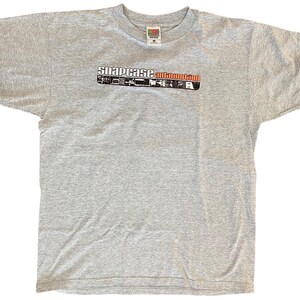 May include: A heather gray t-shirt with the text "snapcase automotrip" in a horizontal design across the chest. The text is in white, black, and red. The shirt has short sleeves and a crew neck.