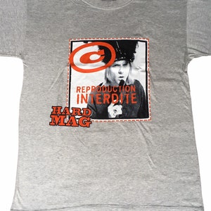 Op de afbeelding: Grijs T-shirt met een rode en witte afbeelding van een vrouw met een hoed en de tekst "Reproduction Interdite" en "Hard Mag".