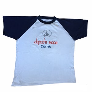 May include: White and navy blue baseball tee shirt with the text "Depeche Mode" and "Exciter" in red and blue lettering. A circle with the letters "DM" is above the text.