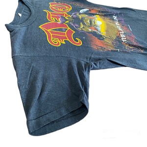 May include: Black t-shirt with a red and yellow graphic of a band logo and the text "The Ultimate Line".