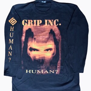 May include: Black long-sleeve t-shirt with a graphic of a face with the text "GRIP INC." and "HUMAN?" on the front. The left sleeve has a graphic of a symbol and the text "HUMAN?"