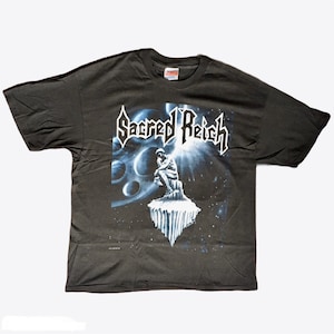 May include: A dark gray t-shirt with a graphic print of a figure sitting on a rock formation in a starry sky. The text "Sacred Reich" is printed in white on the shirt.