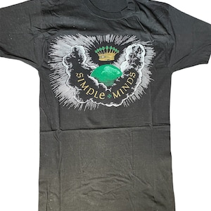 May include: Black t-shirt with a white graphic of a green orb with a gold crown on top, surrounded by clouds and rays of light. The text "SIMPLE MINDS" is written around the orb.
