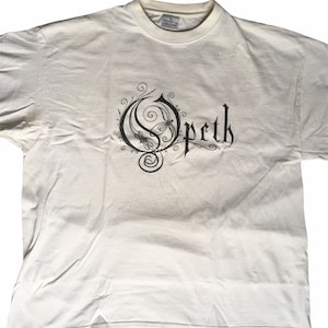 May include: White t-shirt with a black and white graphic of the band "Opeth" in a stylized font with a dragonfly design.