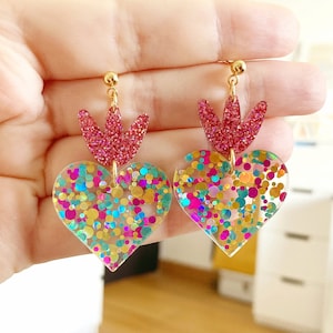 Transparent heart-shaped earring with pink, aqua green, gold, and multicolor glitter, featuring a small tulip, a pink crown, and a round post with an 18k gold-plated stem.