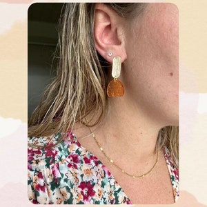 Peut inclure: Une personne portant une chemise à fleurs avec un collier en chaîne dorée et des boucles d'oreilles dorées avec un motif géométrique brun et or