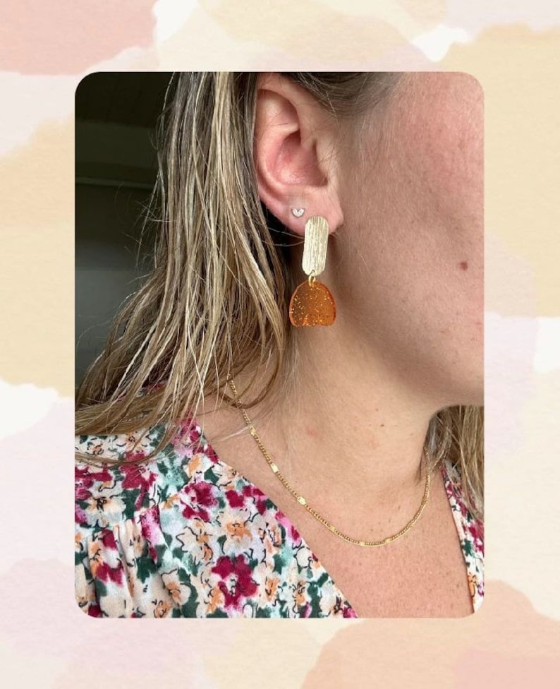 Peut inclure: Une personne portant une chemise à fleurs avec un collier en chaîne dorée et des boucles d'oreilles dorées avec un motif géométrique brun et or