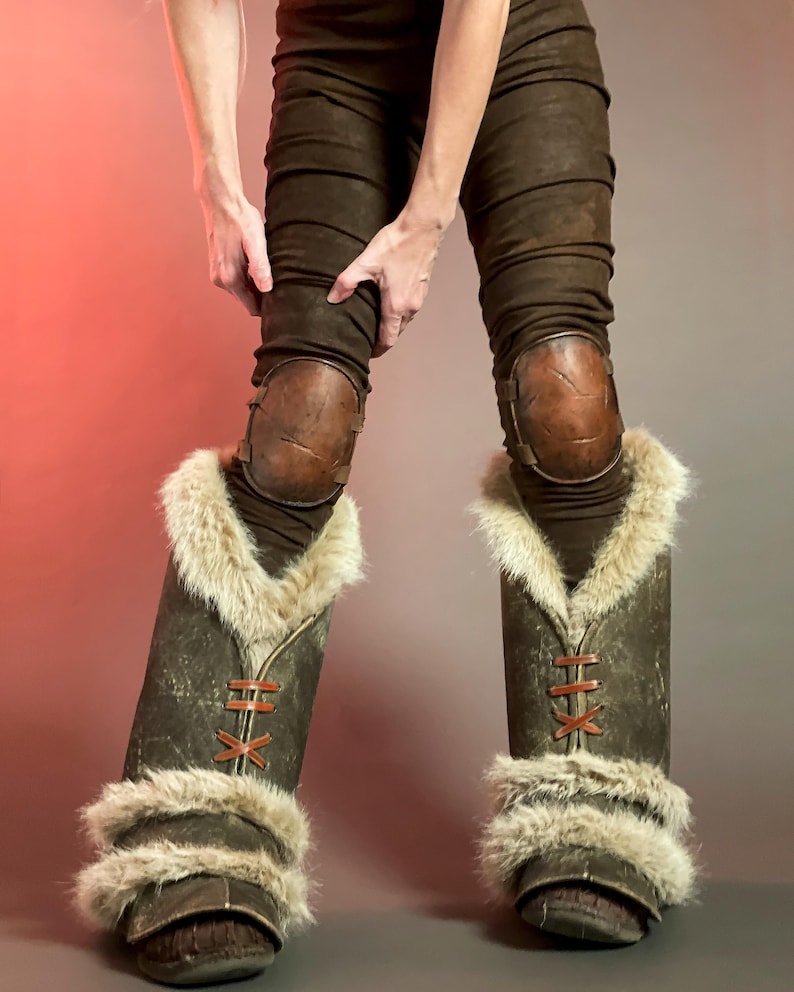May include: Brown leather trousers with knee pads and fur-lined boots. The boots feature a dark brown leather exterior with tan fur trim and red lacing. The knee pads are a lighter brown leather.