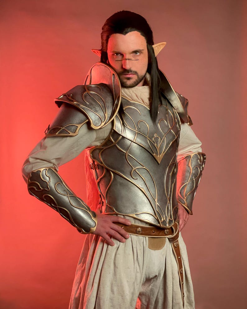 May include: A silver and gold fantasy armor set with intricate designs. The armor includes shoulder pads, a chest plate, and arm guards. The person is wearing a white tunic and a brown belt. The background is a gradient of red.