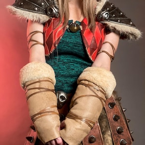 May include: A cosplay costume with a green top, a red and brown diamond-patterned vest, and brown leather details. The costume includes shoulder armour, arm cuffs, and a skirt with fur and metal spikes. The design has a medieval or fantasy theme.
