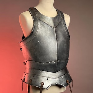 May include: A silver-colored breastplate, displayed on a mannequin. The armor features a detailed design with visible rivets, leather straps, and a decorative trim. The chest piece is designed to protect the torso and is likely part of a medieval or fantasy costume.