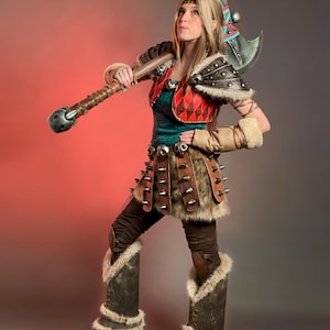 May include: A Viking warrior cosplay costume. The outfit includes a brown and red top, fur-lined boots, and a large axe. The costume has leather accents and metal studs, with a fur trim.