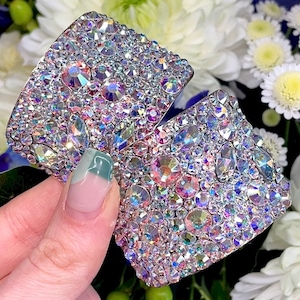 May include: A pair of sparkling, iridescent crystal-covered accessories. The crystals are of various sizes and shapes, reflecting a rainbow of colors. The accessories appear to be a decorative item, possibly for fashion or home decor.