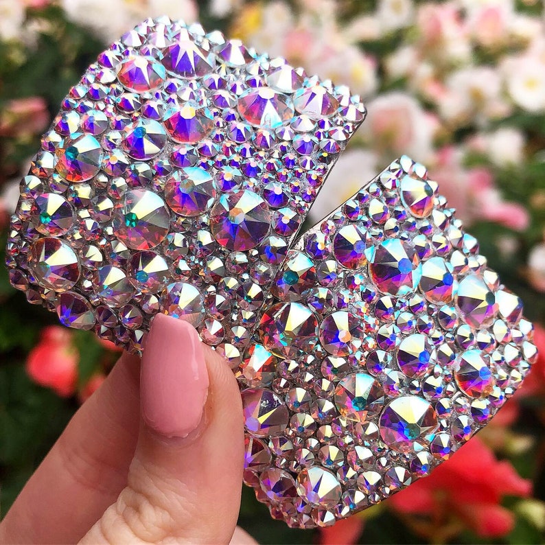 May include: Two silver-toned, crystal-encrusted, decorative pieces. The pieces are shaped like a half-circle and are covered in iridescent rhinestones.