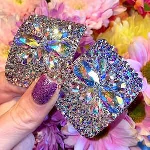 May include: Two silver-toned earrings with a flower design made of iridescent rhinestones.