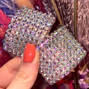 May include: Two square-shaped hair clips covered in iridescent rhinestones. The clips are silver-toned and have a smooth, polished finish.