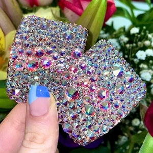 May include: Two square-shaped, iridescent pink and clear crystal embellishments. The crystals are set in a flat, square shape and are perfect for adding sparkle to any project.