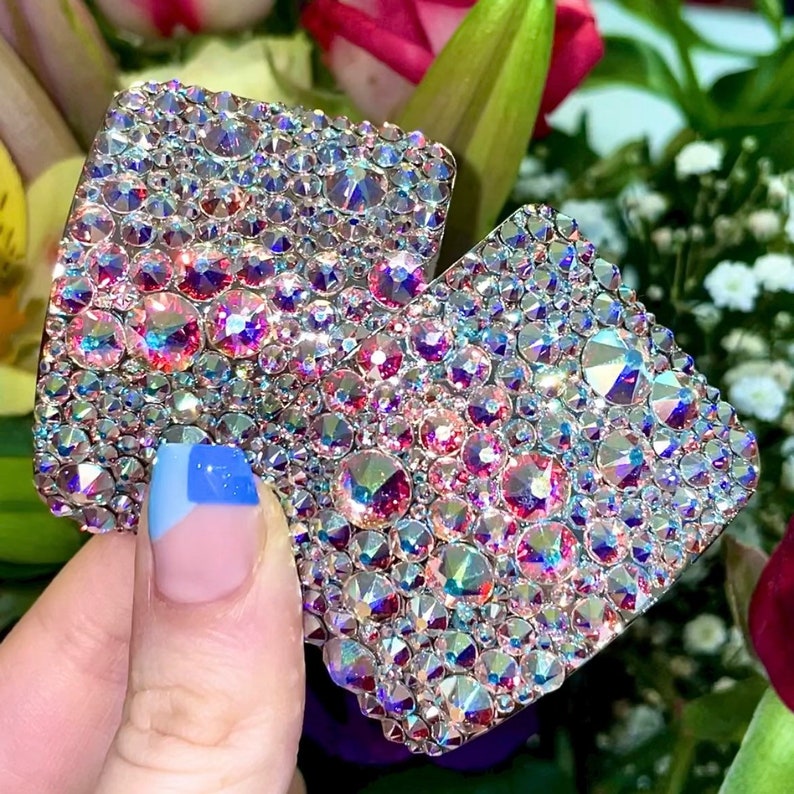 May include: Two square-shaped, iridescent pink and clear crystal embellishments. The crystals are set in a flat, square shape and are perfect for adding sparkle to any project.