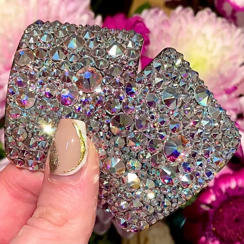 May include: Two heart-shaped pieces of jewelry covered in iridescent rhinestones. The rhinestones are arranged in a random pattern and create a sparkling effect.