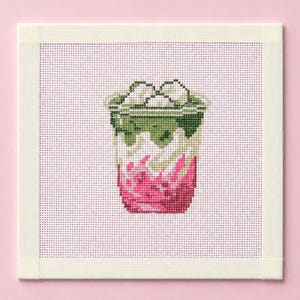 Puede incluir: Un lienzo cuadrado de punto de aguja con un diseño de punto de cruz de una bebida helada en capas dentro de un vaso transparente. La bebida muestra una capa superior verde oscuro, una capa media blanca y una base de color rosa intenso.