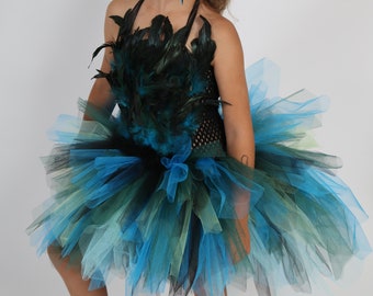 May include: A halter-style dress with a black bodice and a layered tulle skirt in shades of blue, green, and black. The bodice is adorned with black and teal feathers. A blue bow accents the waist, creating a whimsical look.
