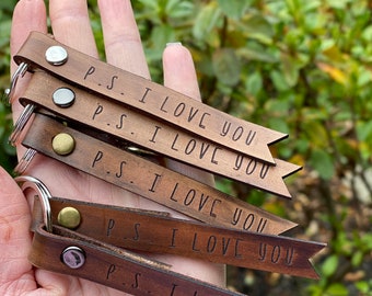 May include: Five brown leather keychains with metal rings and a silver rivet. Each keychain has the text "P.S. I LOVE YOU" engraved on it.