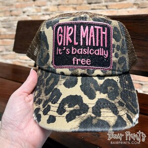 May include: A brown and black leopard print trucker hat with a pink patch that says "Girl Math It's basically free".