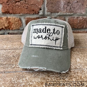 May include: A green and white trucker hat with a distressed look. The hat has a white mesh back and a patch on the front that says "made to worship".