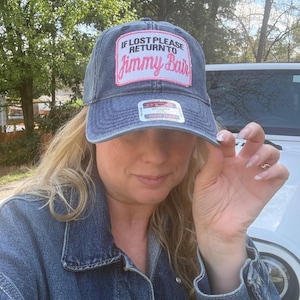 May include: A denim baseball cap with a pink patch that reads "If Lost Please Return to Jimmy Bair." The cap has a curved brim and a distressed look. The hat also has a white tag.