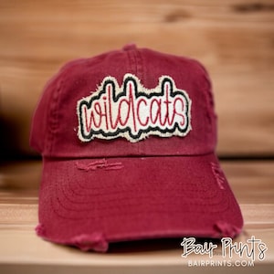 May include: A maroon distressed baseball cap with a white, red, and black embroidered patch that says "Wildcats".