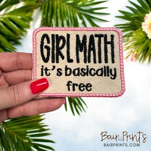 May include: An embroidered patch in beige with pink stitching. The patch reads "Girl Math it's basically free".
