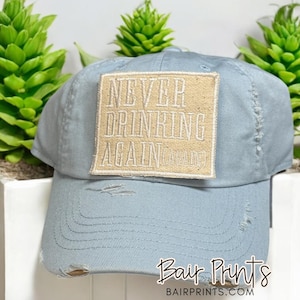 May include: A light blue distressed baseball cap with a beige patch that reads "Never Drinking Again (again)".