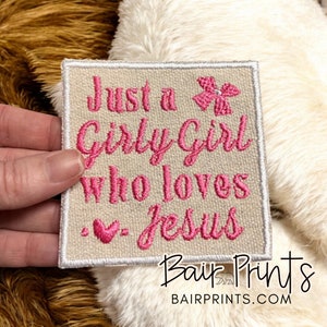 May include: A beige fabric patch with pink embroidery that reads "Just a Girly Girl Who Loves Jesus" with a pink heart and a pink flower.