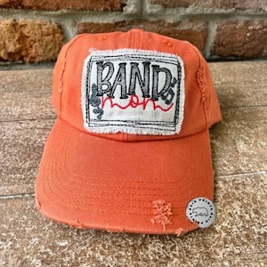 May include: Orange baseball cap with a distressed look and a black and white patch that says "Band Mom" with a musical note and a heart.