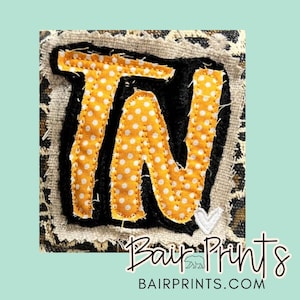 May include: A square patch with the letters "TN" in orange with white polka dots, outlined in black. The patch is set against a leopard print background. The text "Bair Prints" and "bairprints.com" is also visible, along with a small white heart.