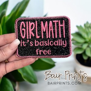May include: A black and pink embroidered patch with the text "Girl Math It's basically free".