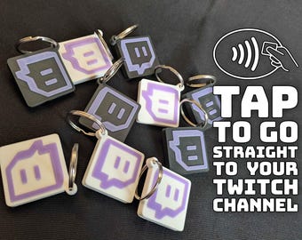 以下が含まれることがあります： 黒、白、紫色のTwitchロゴが入ったキーホルダー。各キーホルダーは正方形で、銀色のキーリングが付いています。画像には「TAP TO GO STRAIGHT TO YOUR TWITCH CHANNEL」というテキストが含まれています。